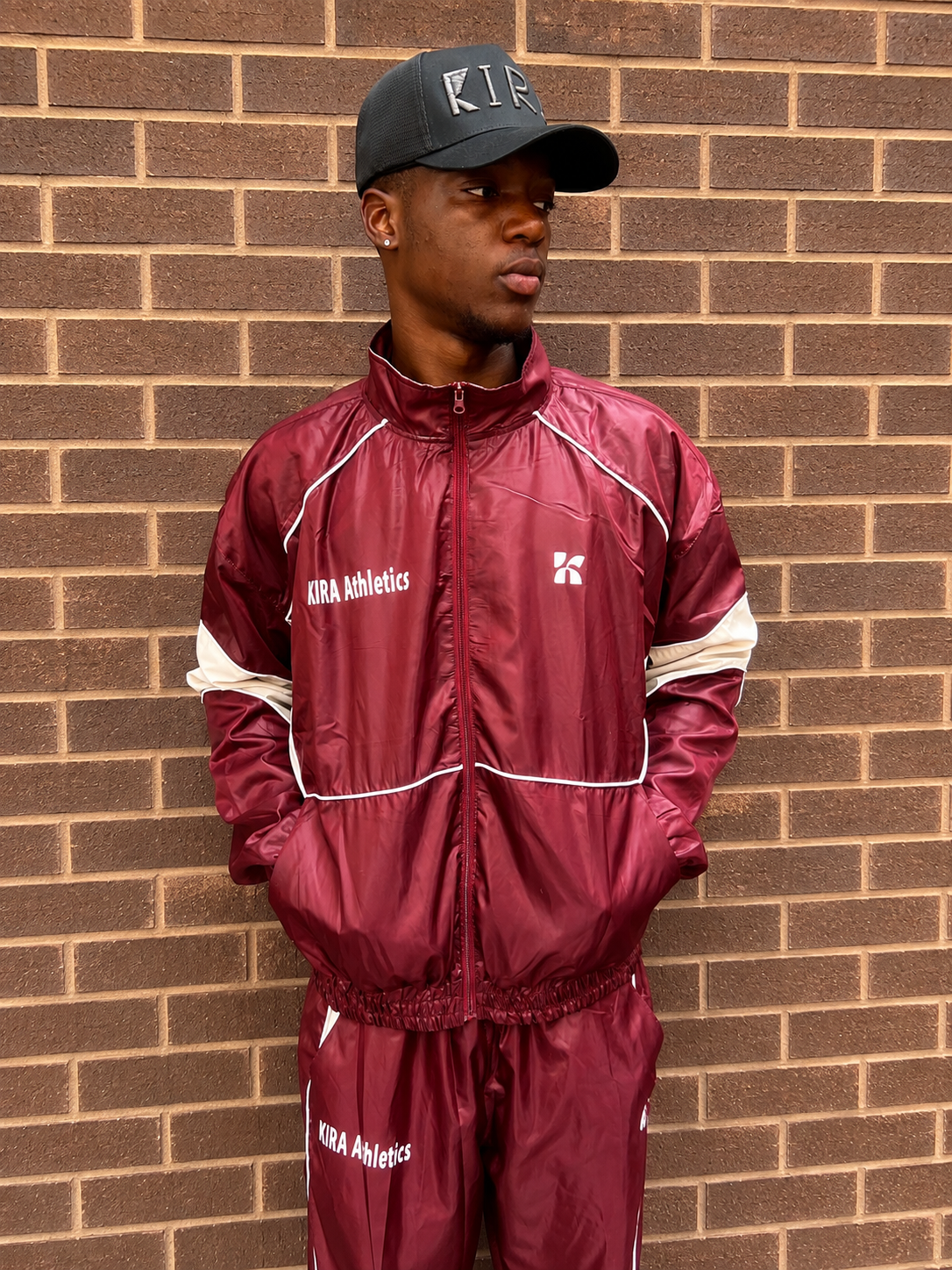 Homme portant le KIRA Tracksuit bordeaux avec veste zippée et pantalon assorti, collection streetwear KIRA Athletics.